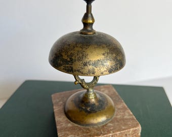 May include: A small brass bell with a marble base. The bell has a tarnished finish and a decorative handle.
