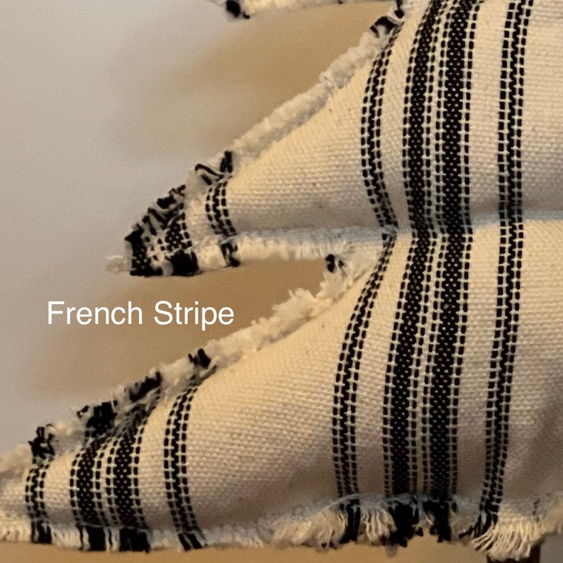 Pu&ograve; includere: Primo piano di un tessuto bianco con strisce nere. Il tessuto ha un bordo sfrangiato e il testo "French Stripe" &egrave; visibile nell'immagine.