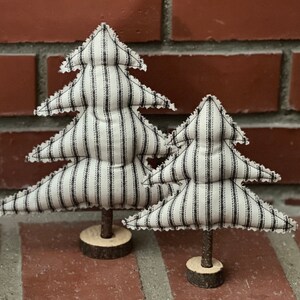 Pu&ograve; includere: Due alberi di Natale in tessuto a righe bianche e nere con una base in legno rustica.