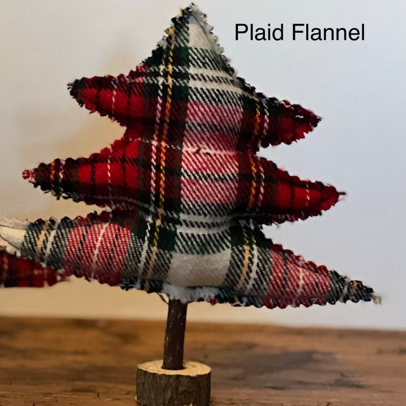 Pu&ograve; includere: Un piccolo albero di Natale in flanella a quadri rossi e verdi con una base in legno marrone. L'albero &egrave; decorato con un motivo a quadri bianchi e gialli. Il testo "Plaid Flannel" &egrave; scritto sopra l'albero.