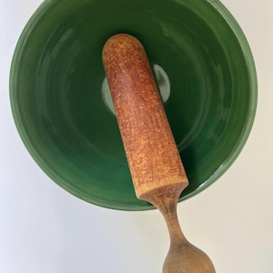 May include: A green ceramic bowl with a wooden pestle. The bowl has a swirling pattern and the pestle has a rounded handle.