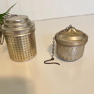 May include: Two vintage silver tea infusers. One is cylindrical with a chain and hook, the other is round with a decorative top and chain. Both have small holes for steeping tea leaves.