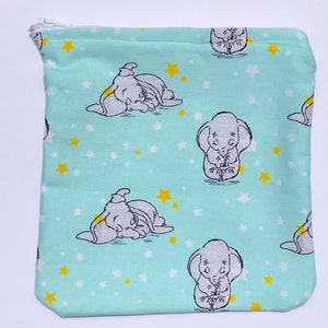 May include: A square, zipped pouch with a light teal background. The pouch features illustrations of Dumbo the elephant and yellow and white stars. The zipper is white. The pouch is suitable for storing small items.