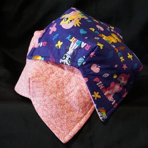 Puede incluir: Dos salvamanteles cuadrados de tela. Uno es rosa con un estampado de hojas blancas. El otro es azul oscuro con ponis de dibujos animados, corazones y estrellas. Las palabras "Pinkie Pie" y "Rarity" son visibles.