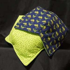 Puede incluir: Una almohada verde y azul con un patrón de hojas verdes y camaleones azules. La almohada está hecha de tela y tiene una textura suave y cómoda.