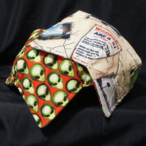 May include: A baseball cap with a white and brown map pattern on the front and a green alien pattern on the back. The map pattern includes the text "WARNING AREA 51 Restricted Area".