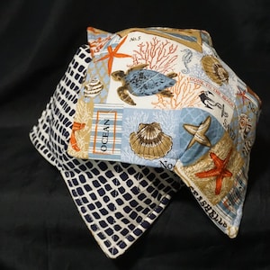 Puede incluir: Un juego de dos agarraderas de olla azul y blanco con temática náutica. Las agarraderas presentan una variedad de vida marina, incluyendo una tortuga, una estrella de mar, conchas y coral. El texto "Gone to the Beach" y "No. 5" está impreso en las agarraderas.