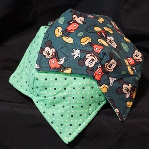 May include: Two fabric bowl cozies. One is teal with a Mickey Mouse pattern, the other is mint green with white polka dots. The cozies are square and quilted, designed to be placed in the microwave.