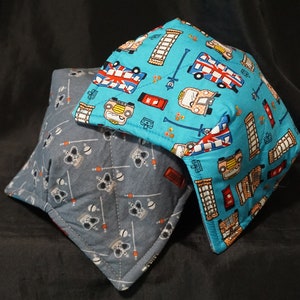 May include: Two fabric pot holders. One is blue with a pattern of red, white, and blue double-decker buses, red mailboxes, and red telephone booths. The other is gray with a pattern of white crowns and sticks.