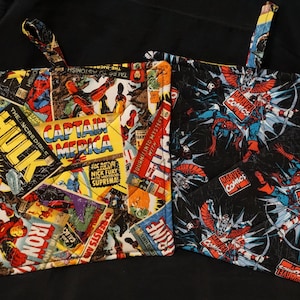 Puede incluir: Dos agarraderas cuadradas acolchadas. Una presenta un collage de portadas de cómics con personajes como Hulk, Capitán América e Iron Man. La otra es negra con un patrón de personajes de Marvel Comics. Ambas tienen lazos para colgar.