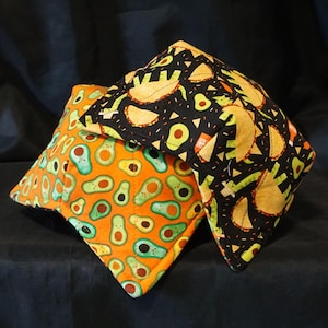 May include: Two fabric pillow covers with a black background and a pattern of avocados and tacos. One pillow cover is orange with a pattern of avocados.