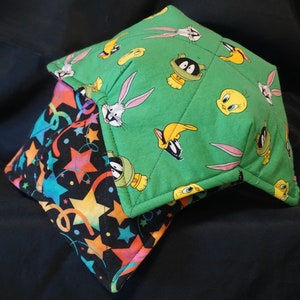 May include: A green and black fabric bowl cosy with a cartoon character pattern. The pattern includes Bugs Bunny, Tweety Bird, and Sylvester the Cat. The cosy is quilted and has a star and confetti pattern on the inside.