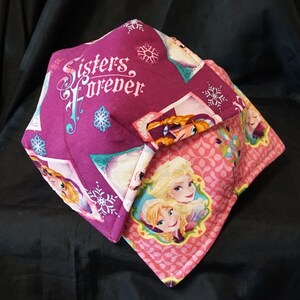 May include: A purple and pink fabric bowl with a quilted design. The bowl features a print of the characters from the movie Frozen, including Elsa and Anna. The text "Sisters Forever" is printed on the bowl.