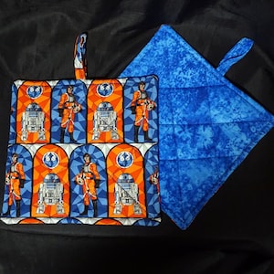 May include: A set of two Star Wars themed pot holders. One is blue with a quilted design and the other is a colorful print featuring characters from the Star Wars franchise.