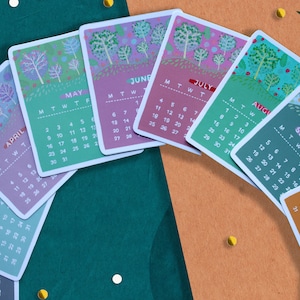 Peut inclure: Plusieurs calendriers mensuels illustr&eacute;s, chacun affichant un mois diff&eacute;rent, comme mai, juin et juillet. Les calendriers sont dispos&eacute;s en demi-cercle, avec des illustrations de paysages. Le fond est un m&eacute;lange de vert et d'orange.