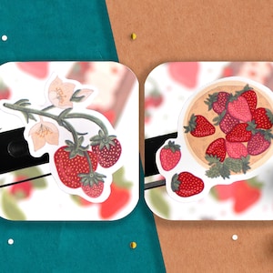 May include: Two stickers featuring illustrations of strawberries. The first sticker shows a strawberry plant with white flowers and red strawberries. The second sticker shows a bowl of red strawberries.