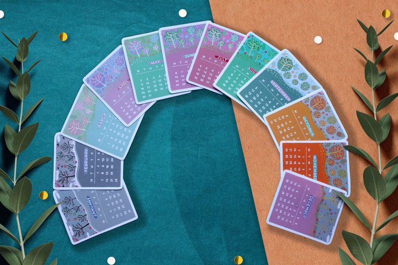 Peut inclure: Un ensemble de douze cartes de calendrier illustr&eacute;es, chacune repr&eacute;sentant un mois de l'ann&eacute;e. Les cartes sont dispos&eacute;es en arc, pr&eacute;sentant des illustrations saisonni&egrave;res color&eacute;es et les dates du calendrier. Le fond est un m&eacute;lange de turquoise et d'orange avec des &eacute;l&eacute;ments d&eacute;coratifs.