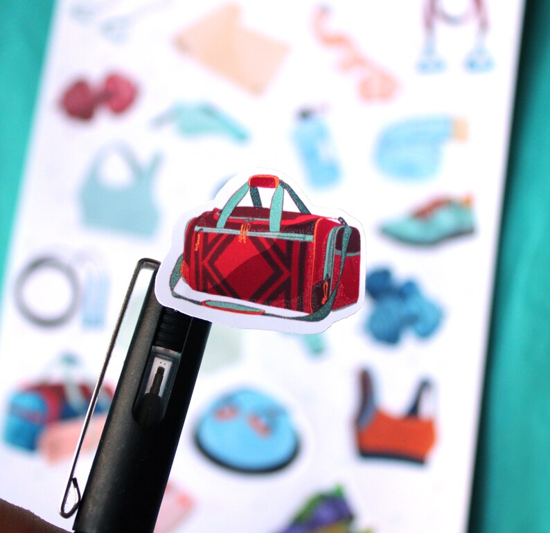 May include: A red and black duffel bag with a teal zipper and handle. The bag is on a white sheet with other stickers.