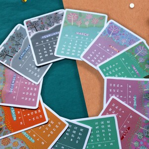 Peut inclure: Un ensemble de cartes de calendrier mensuelles illustr&eacute;es, dispos&eacute;es en cercle. Chaque carte pr&eacute;sente un mois diff&eacute;rent avec un motif d'arbre saisonnier unique et le nom du mois. La palette de couleurs comprend des verts, des oranges et des violets.