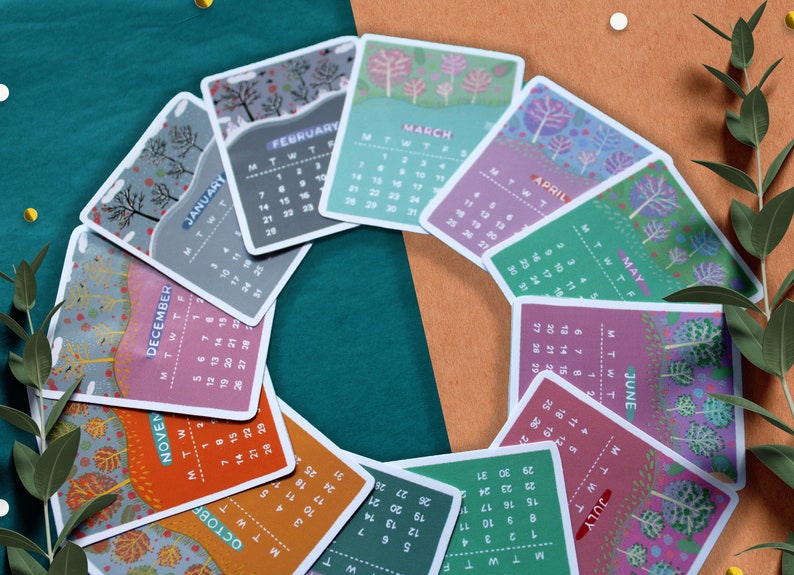 Peut inclure: Un ensemble de cartes de calendrier mensuelles illustr&eacute;es, dispos&eacute;es en cercle. Chaque carte pr&eacute;sente un mois diff&eacute;rent avec un motif d'arbre saisonnier unique et le nom du mois. La palette de couleurs comprend des verts, des oranges et des violets.