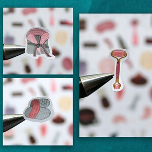 May include: Three stickers featuring beauty and self-care items. The first sticker shows a pink and gray headband with a bow. The second sticker shows a pink and gold facial roller. The third sticker shows a pair of pink and gray slippers.