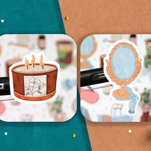 May include: Two stickers on a white background. The sticker on the left is a candle with a floral design and three flames. The sticker on the right is a gold mirror with a blue reflection and a pearl necklace.