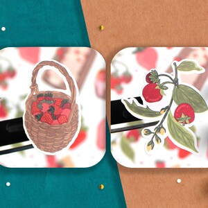 May include: Two stickers featuring illustrations of strawberries. One sticker shows a wicker basket overflowing with red strawberries. The other sticker shows a branch of green leaves with red strawberries.