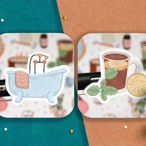 May include: Two illustrated stickers, one of a blue bathtub with a pink towel and a shower head, and the other of a brown mug with a lemon slice and green mint leaves.