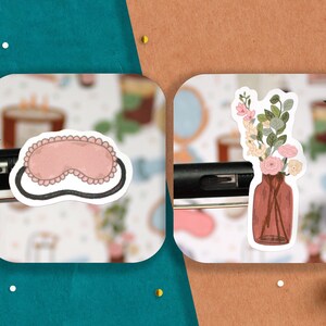 May include: Two stickers, one with a pink sleep mask and the other with a vase of flowers. The sleep mask is black with pink trim and the vase is brown with pink and white flowers.