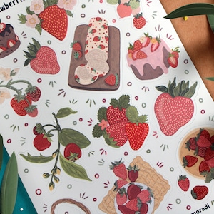 May include: A sheet of stickers featuring various illustrations of strawberries, including a strawberry roll cake, a strawberry cake, and a bowl of strawberries. The stickers are on a white background with a green border.