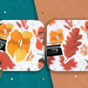 May include: Two autumn-themed stickers featuring a cluster of yellow and orange leaves and a single red oak leaf.