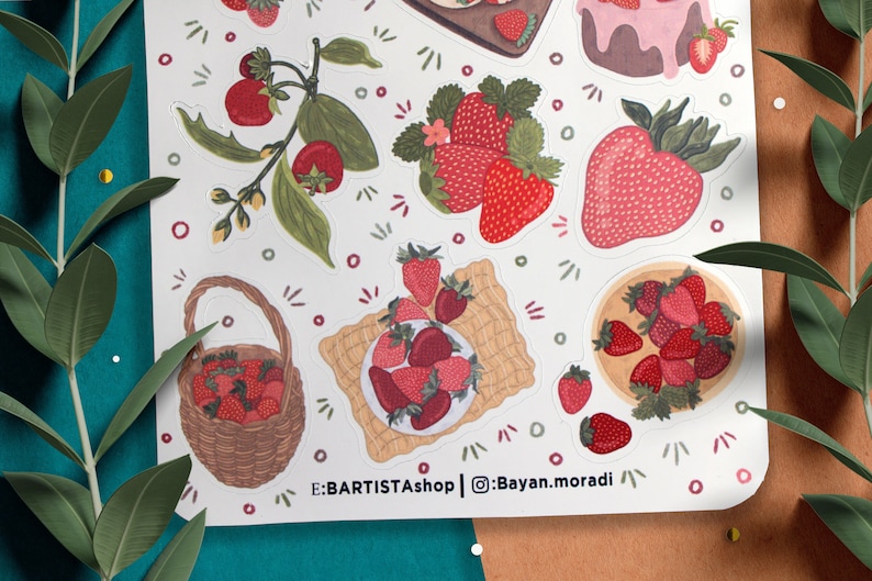 May include: A sheet of stickers featuring various illustrations of strawberries, including a basket full of strawberries, a plate of strawberries, and a strawberry plant with leaves and flowers. The stickers are on a white background with a light brown border. The text "E:BARTISTAshop | @Bayan.moradi" is printed at the bottom of the sheet.