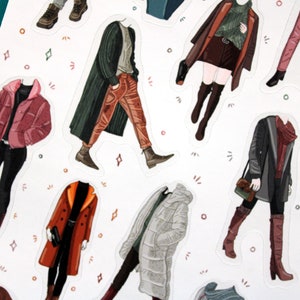 May include: A set of 10 illustrated stickers featuring different outfits for paper dolls. The stickers are printed on white paper and feature a variety of colors and patterns.