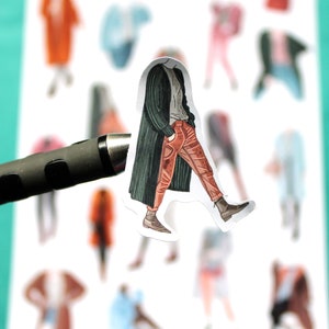 May include: A sticker of a person wearing a green jacket and red pants walking. The sticker is on a white background with other stickers of people in different outfits.