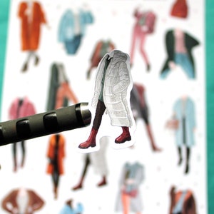 May include: A white puffer jacket with a black trim and red boots. The jacket is part of a set of paper doll stickers.
