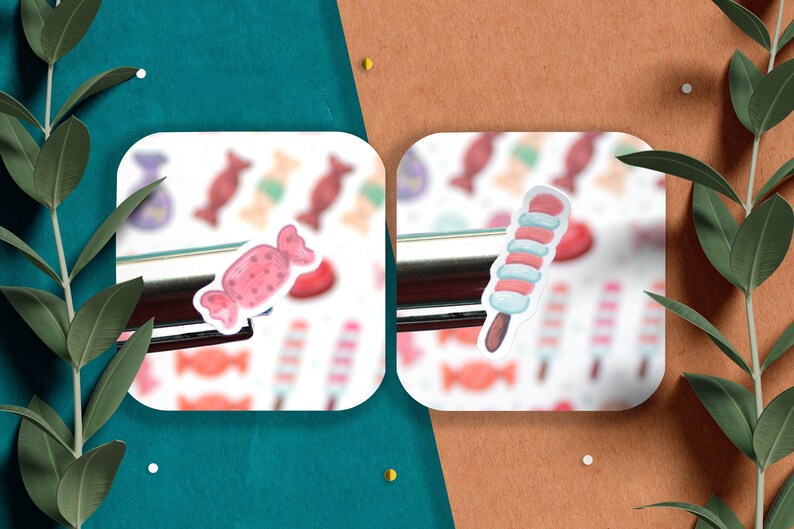 May include: Two white square stickers with a pink and white candy and a blue and white candy on a brown surface. The stickers are surrounded by green leaves.