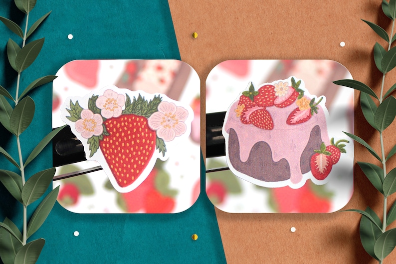 May include: Two stickers featuring strawberry designs. The first sticker shows a single strawberry with pink flowers and green leaves. The second sticker shows a strawberry cake with pink frosting and strawberries on top.