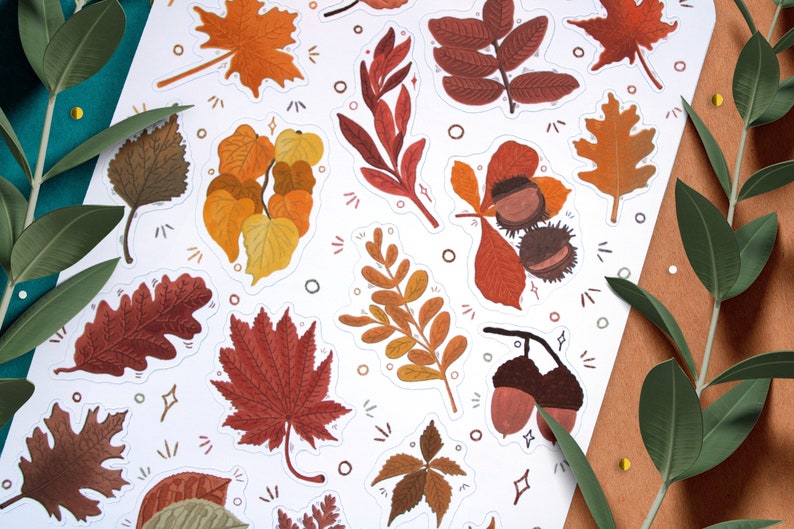 May include: A set of 12 autumn-themed stickers featuring various leaves and acorns in shades of brown, orange, yellow, and red. The stickers are on a white background with a decorative pattern of dots and lines.