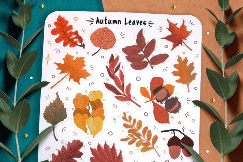 May include: A sheet of stickers featuring various autumn leaves in shades of red, orange, yellow, and brown. The stickers are arranged in a grid pattern and have a white background. The text "Autumn Leaves" is printed at the top of the sheet.