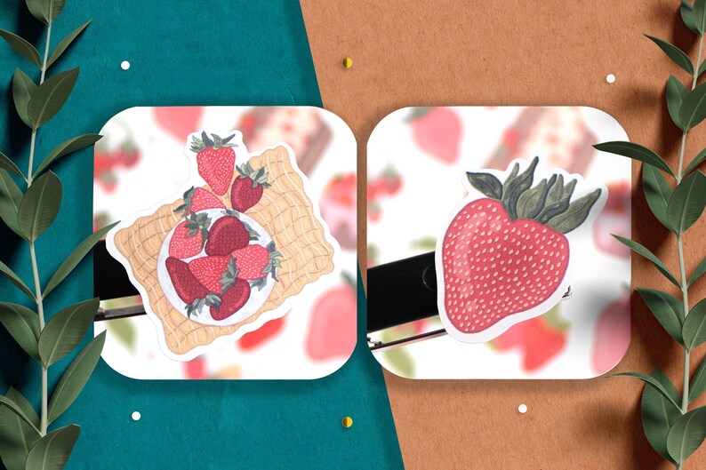 May include: Two stickers featuring illustrations of strawberries. The first sticker shows a plate of strawberries on a woven mat. The second sticker shows a single strawberry with green leaves.