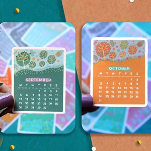 Peut inclure: Deux petites cartes de calendrier, une pour septembre et une pour octobre, sont affich&eacute;es. La carte de septembre a un fond vert avec un motif d'arbres. La carte d'octobre a un fond orange avec un motif d'arbres. Les cartes sont entour&eacute;es de feuilles vertes et de confettis.