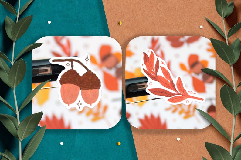 May include: Two stickers featuring autumnal designs. One sticker shows two brown acorns with pink caps. The other sticker shows a branch with red leaves.