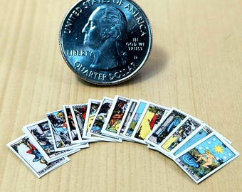 May include: Miniature tarot cards with colorful illustrations are fanned out on a wooden surface. A US quarter coin is positioned above the cards. The cards feature various images and text, showcasing a mystical theme.