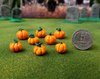 May include: Eight miniature orange pumpkins with green stems, arranged on a green surface. A US quarter is included for scale.
