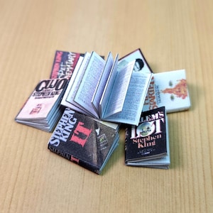Op de afbeelding: Een verzameling miniatuur paperback boeken van Stephen King, waaronder "It", "Salem's Lot", "Cujo", "Pet Sematary" en "Carrie".