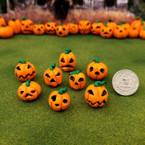 May include: A collection of nine small orange ceramic pumpkins with green stems and carved faces. The pumpkins are arranged on a green surface.