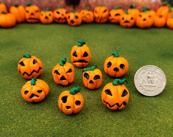 May include: A collection of nine small orange ceramic pumpkins with green stems and carved faces. The pumpkins are arranged on a green surface.