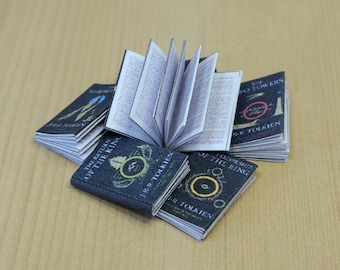 May include: A set of five miniature hardcover books with black covers and gold lettering. The books are titled "The Fellowship of the Ring", "The Two Towers", and "The Return of the King".