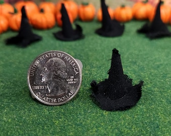 May include: A black witch hat made of fabric with a frayed edge, next to a US quarter dollar coin. The hat is about the size of the coin.