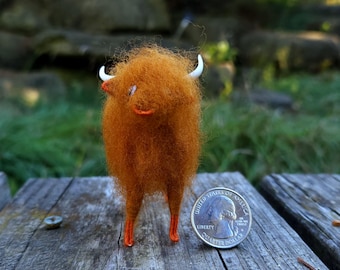 May include: A handmade orange felted bull figurine with white horns and orange feet. The bull is standing on a wooden surface next to a U.S. quarter coin. The bull has a smiling face and a shaggy appearance.